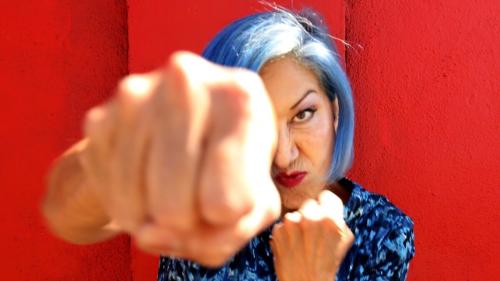 a woman with blue hair punching towards the camera